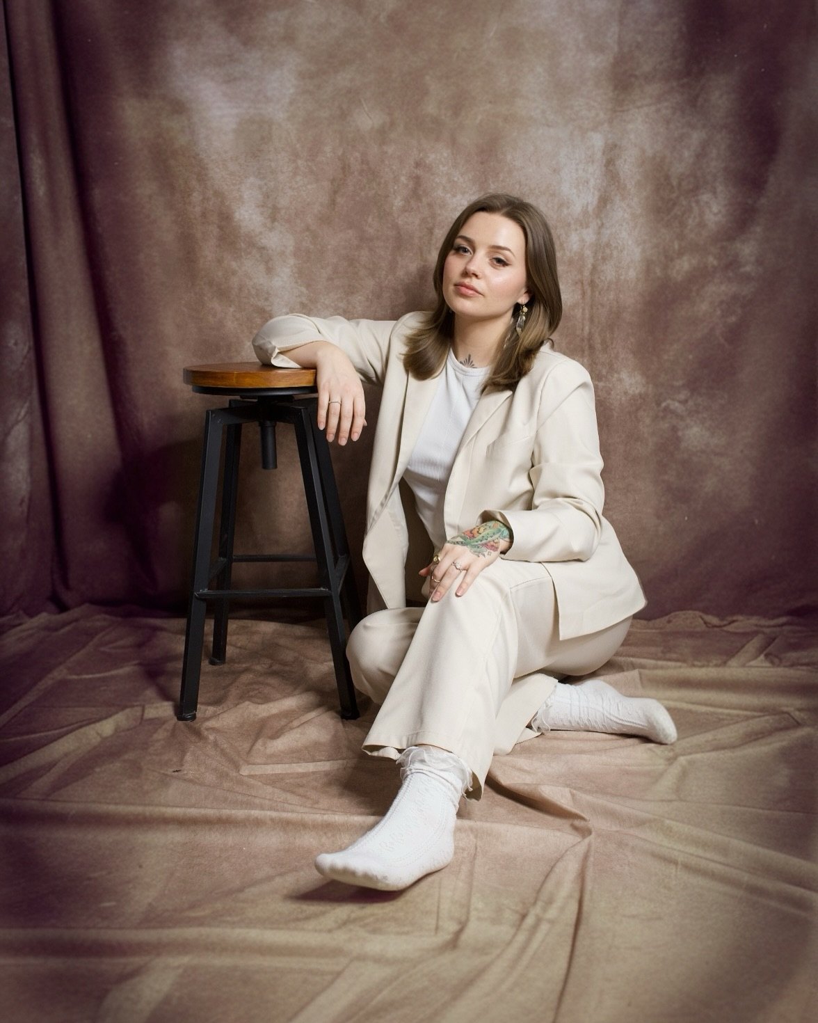 Jenna Feezel seated in a cream suit against a painted backdrop