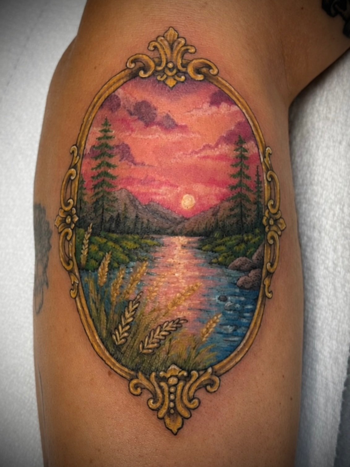 Colour tattoo of a pink sunset over a river, framed in an ornate gilt mirror